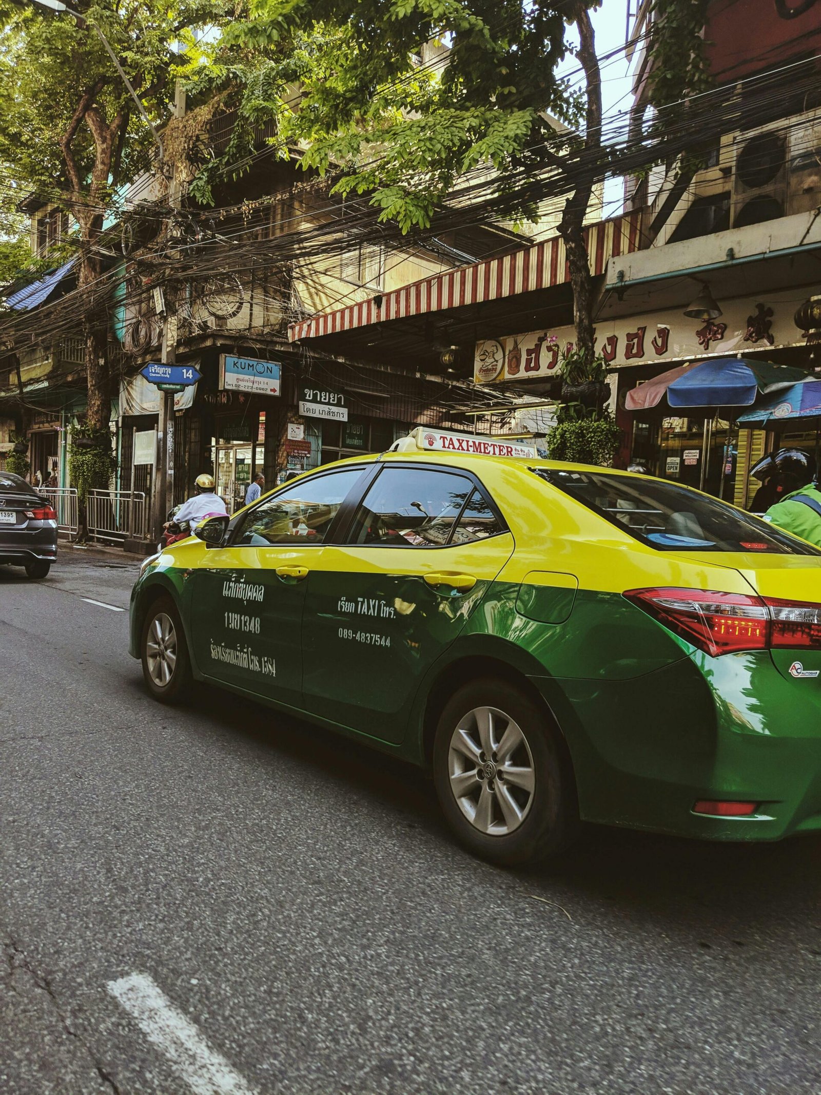 Colorful street view featuring a green and yellow Thai taxi in Samphanthawong, Bangkok.